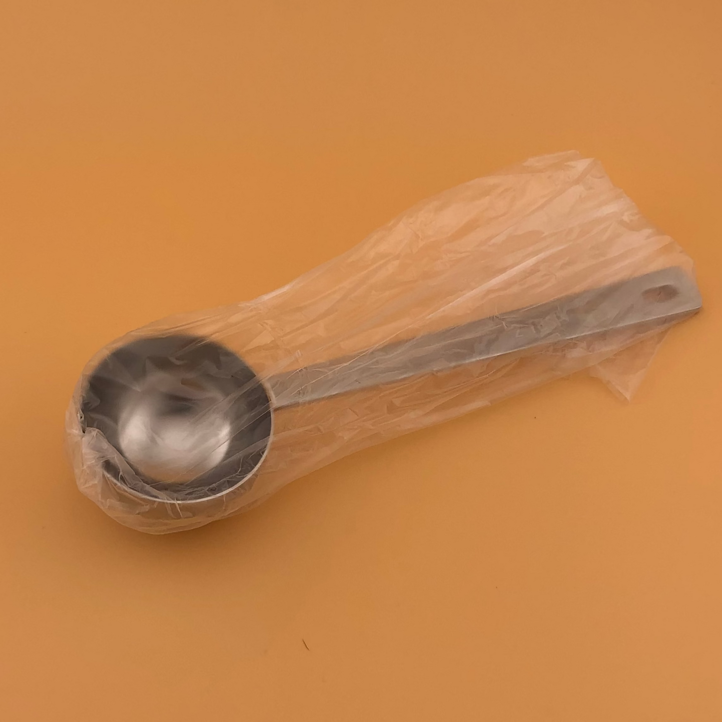 Metal measuring spoon inside a clear plastic bag on an orange background
