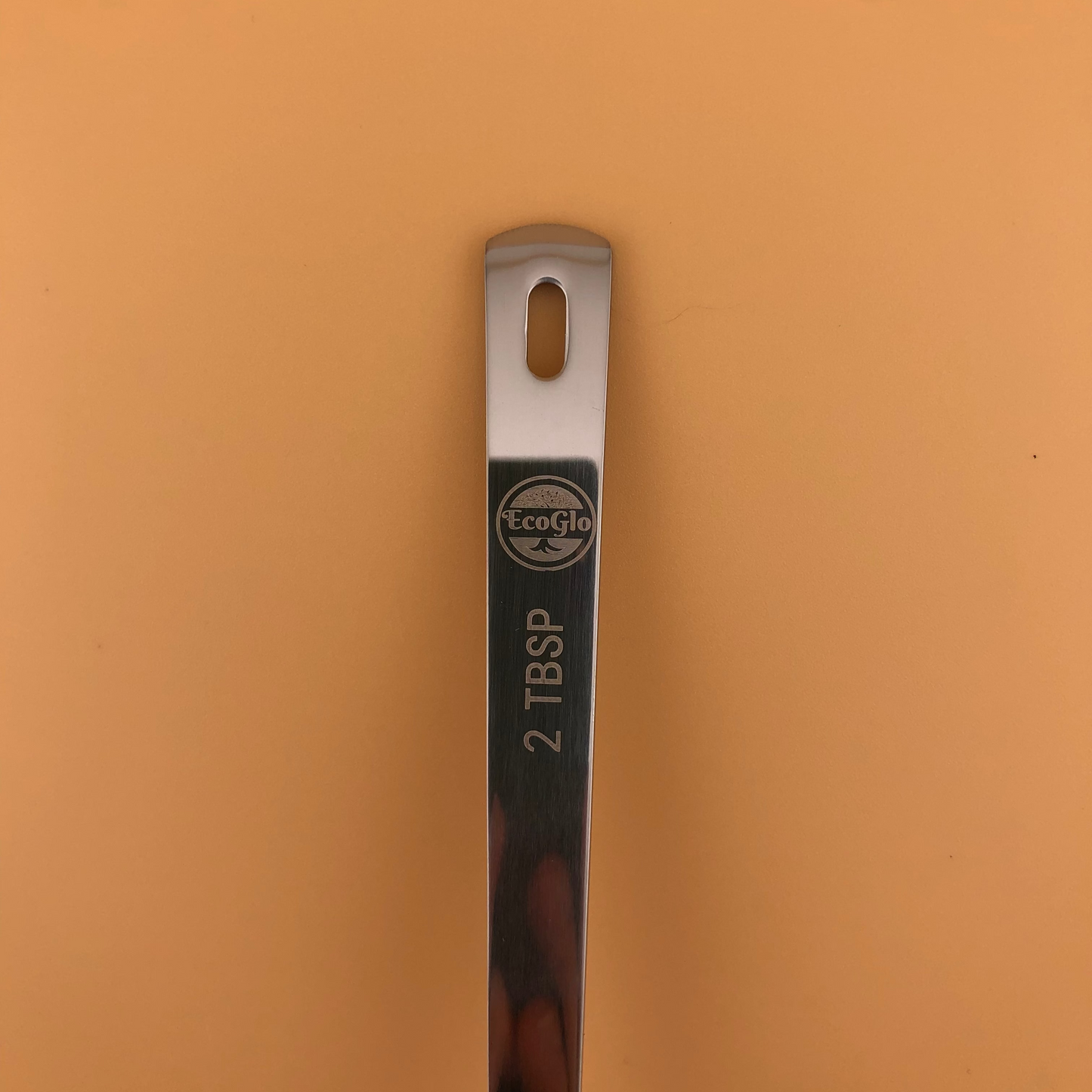 Metal measuring spoon with '2 TBSP' marking on a brown background