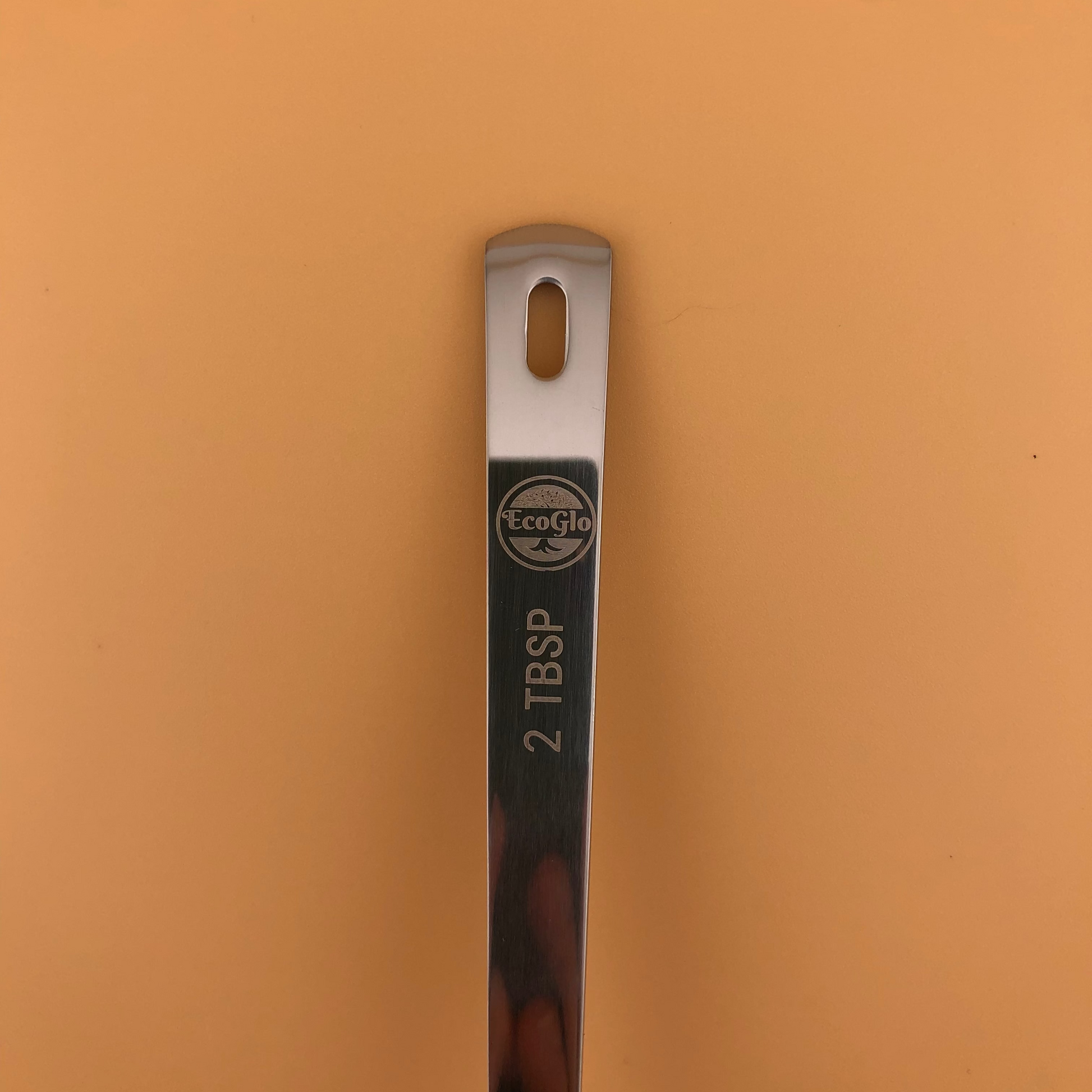 Metal measuring spoon with '2 TBSP' marking on a brown background