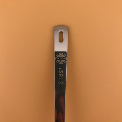 Metal measuring spoon with '2 TBSP' marking on a brown background